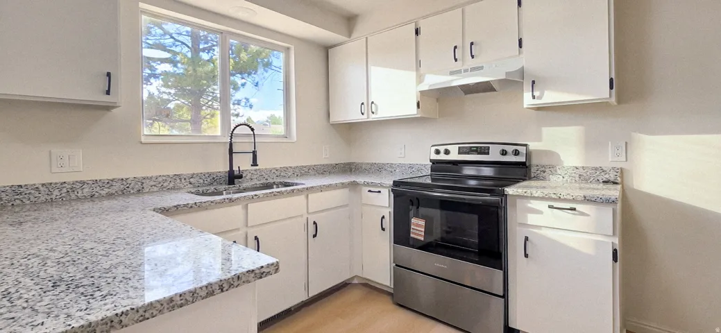 Kitchen featuring white cabinetry, light-toned countertops, stainless steel range, and a single basin sink with a matte black faucet