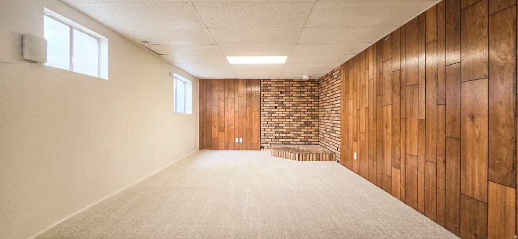Expansive room featuring light-colored carpeting, wood paneling, and a brick accent wall with a raised hearth