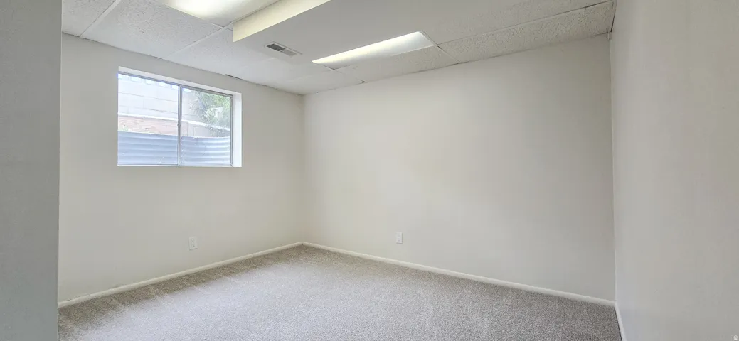 Carpeted room featuring a drop ceiling with recessed lighting and a single window