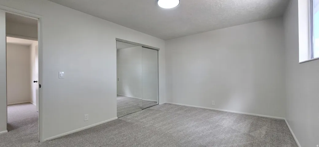 Light-colored carpeting with mirrored closet doors and a flush-mount ceiling light fixture