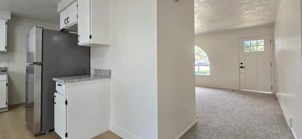 Kitchen area with stainless steel refrigerator, white cabinetry, and granite-look countertops