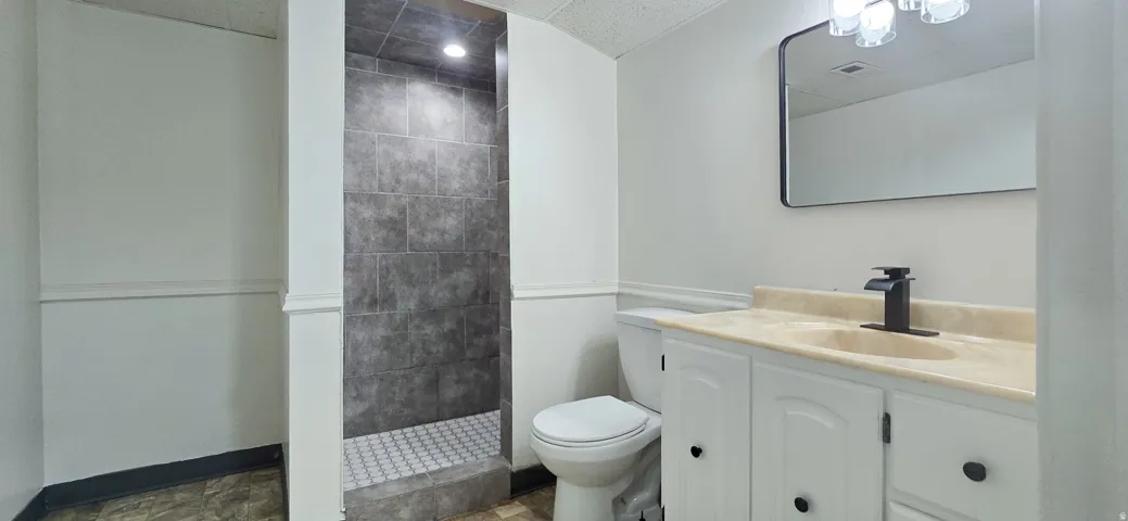 Bathroom featuring a walk-in shower with gray tile surround and hex tile floor, a vanity with a single sink and black faucet, and a wall-mounted mirror