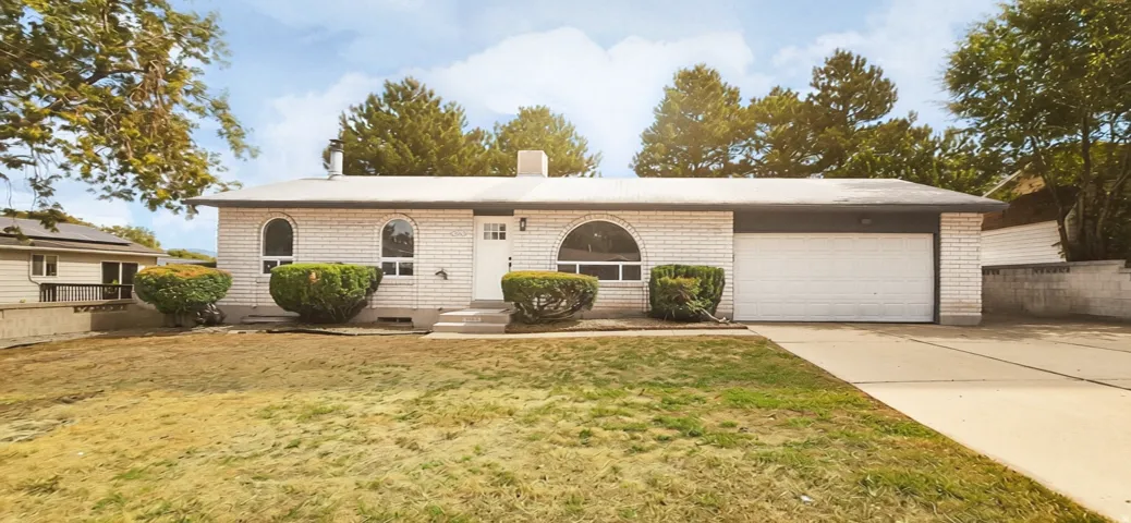 White brick exterior, arched windows, attached garage, concrete driveway, mature landscaping
