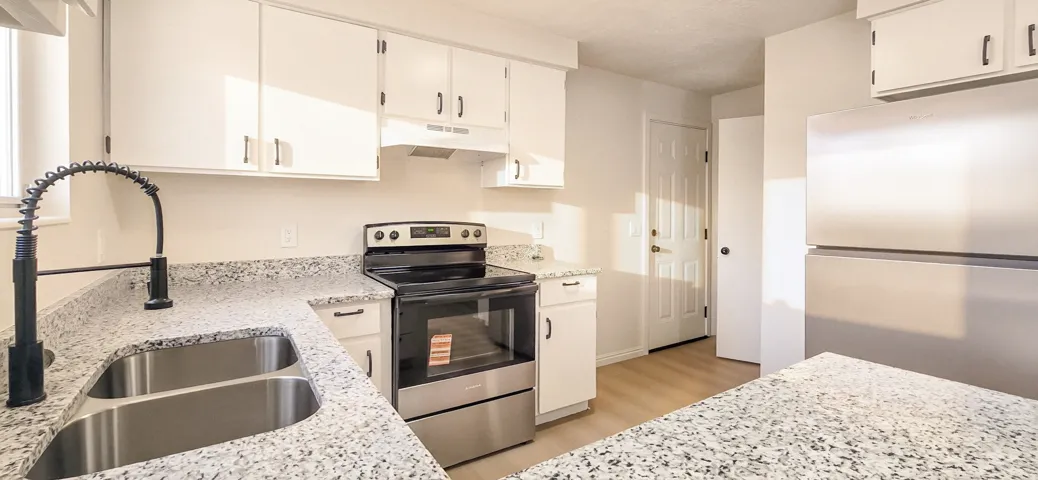 White cabinetry with matte black hardware, dual stainless steel sink, black gooseneck faucet, light-toned wood-finish flooring, and stainless steel appliances