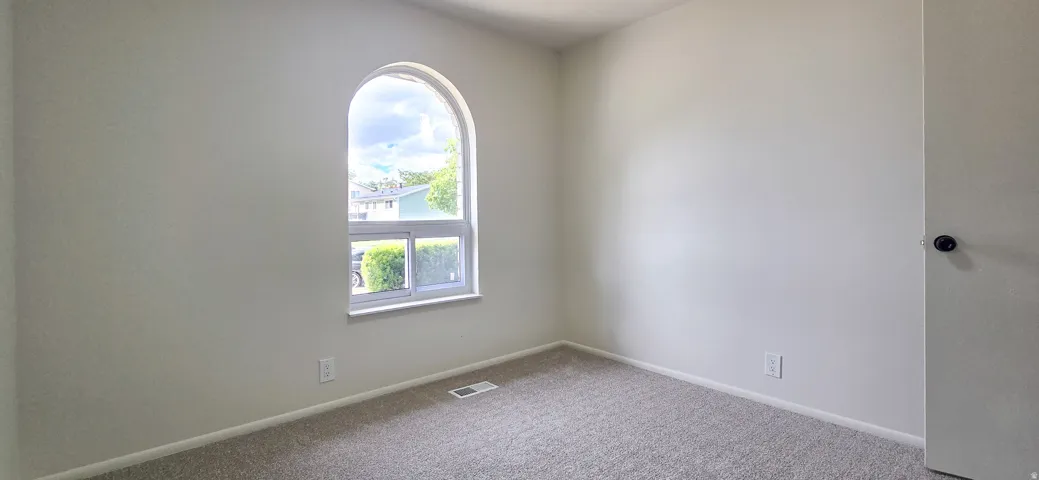 Arched window, light-toned walls, and neutral carpeted flooring