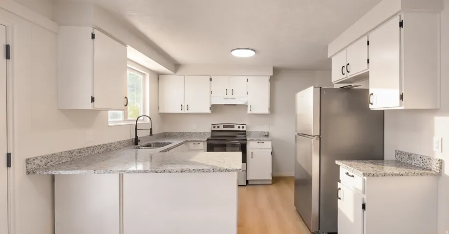 Modern kitchen featuring white cabinetry, light-toned granite countertops, a stainless steel refrigerator, and wood-finish flooring