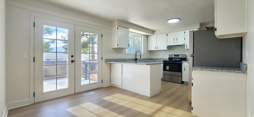 White kitchen cabinetry, stone-finish countertops, stainless steel appliances, wood-finish flooring, and French doors