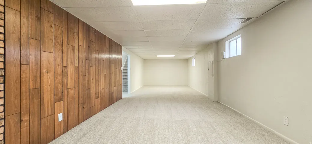 Expansive room featuring wood-finish paneling, light-toned carpeting, and a drop ceiling with recessed lighting