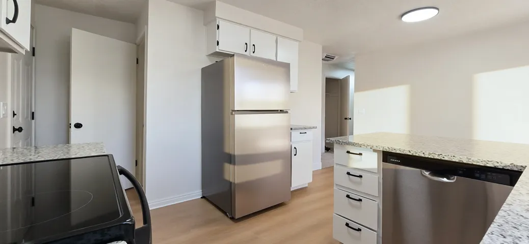 Kitchen featuring granite-style countertops, stainless steel appliances, white cabinetry, and wood-finish flooring