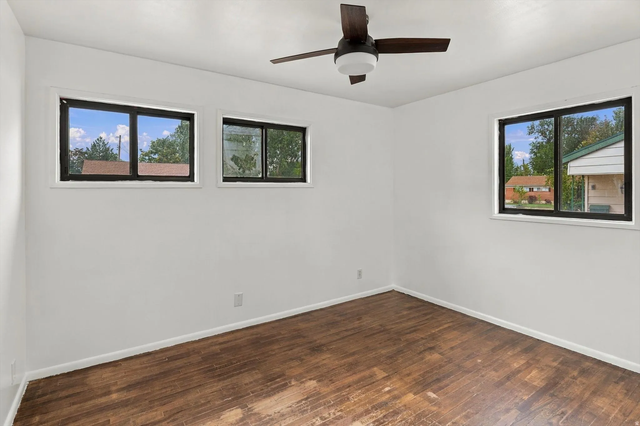 Wood-finish flooring, white painted walls, and a ceiling fan with integrated lighting