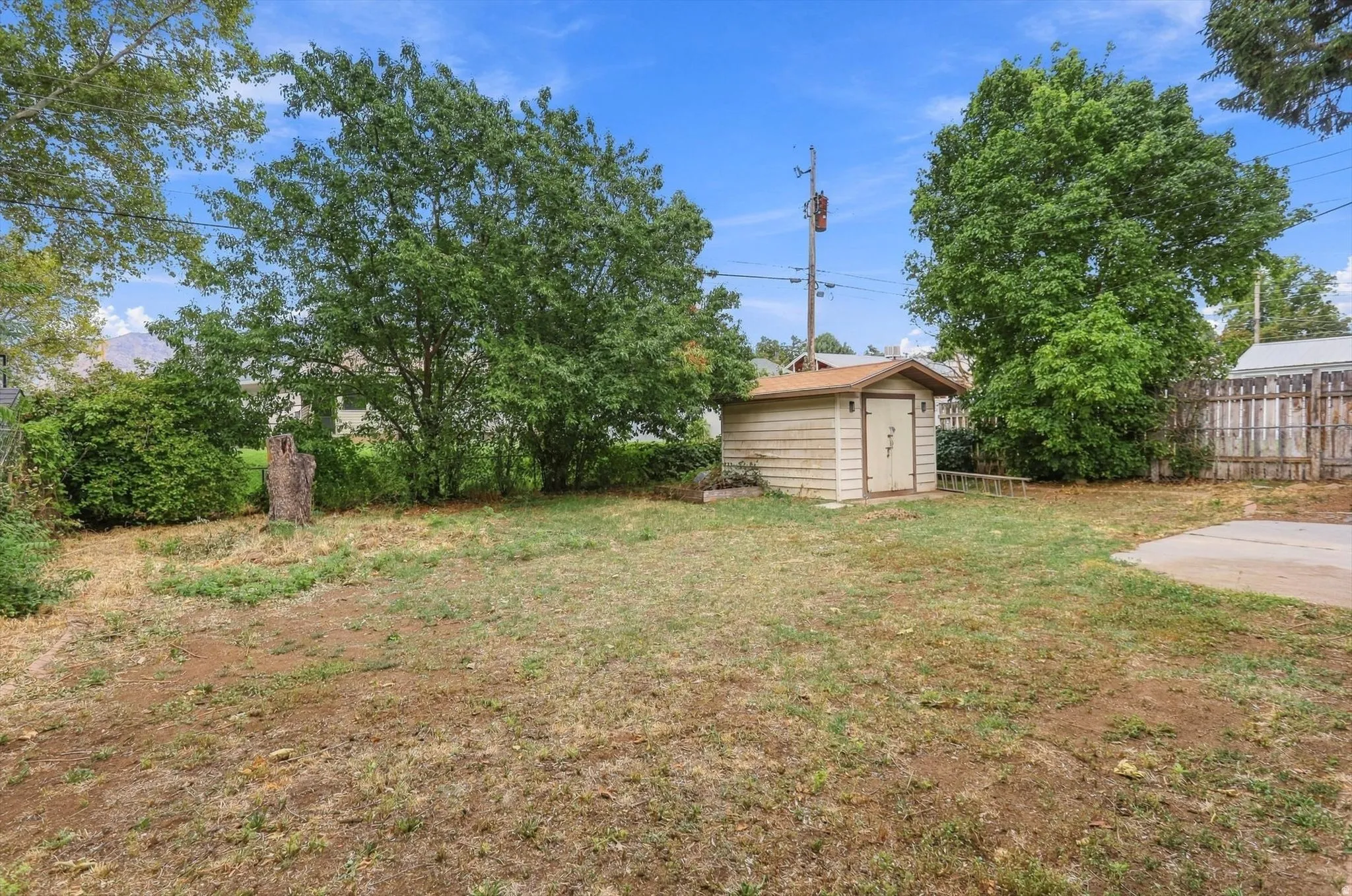 Expansive yard featuring mature trees, a storage shed with double doors, and a concrete pad