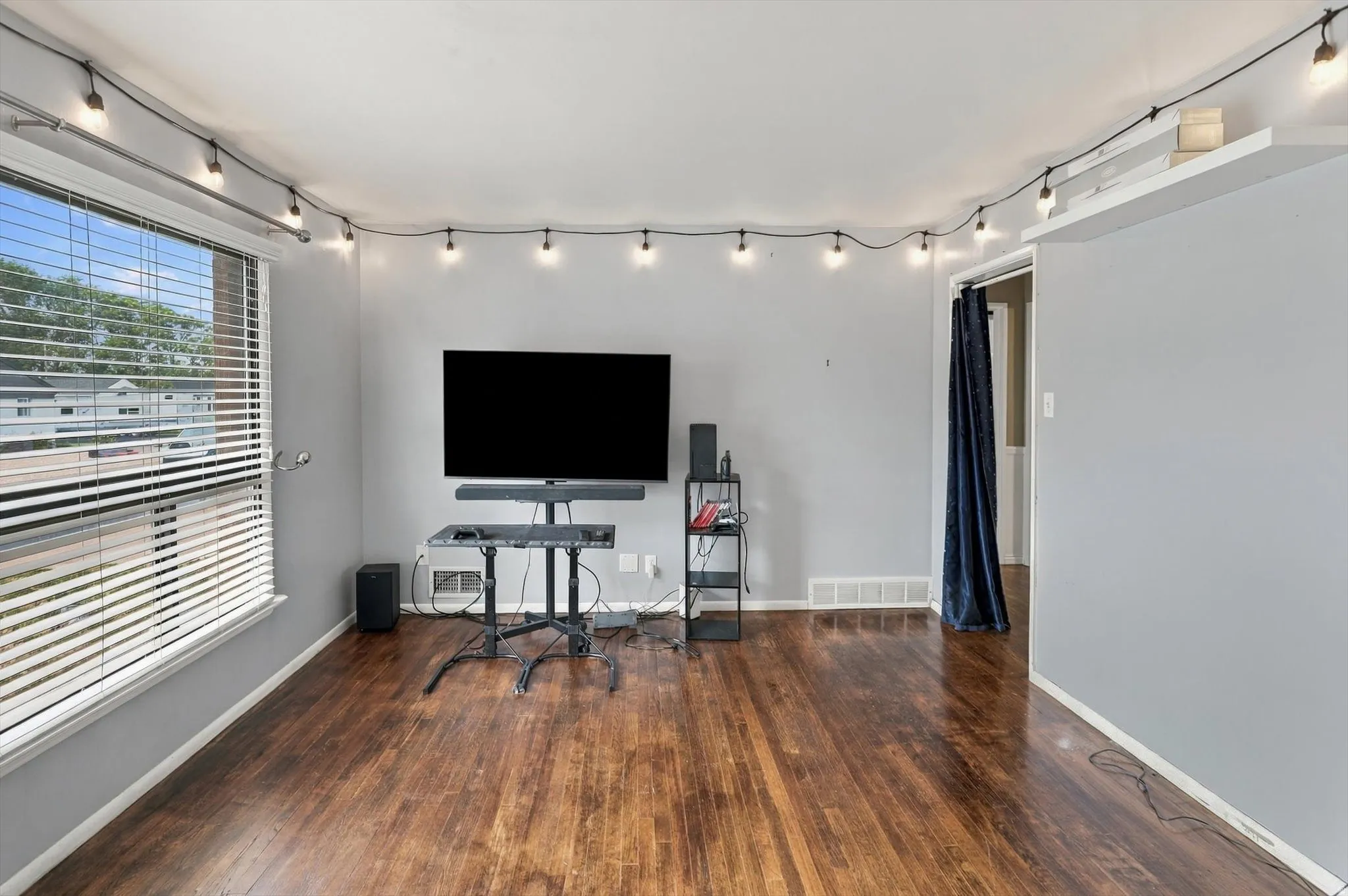 Wood-finish flooring, light gray walls, large window with horizontal blinds, and a doorway