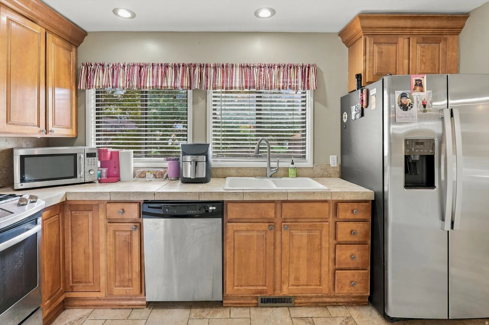 Wood-finish cabinetry, tile countertops, recessed lighting, and a double basin sink