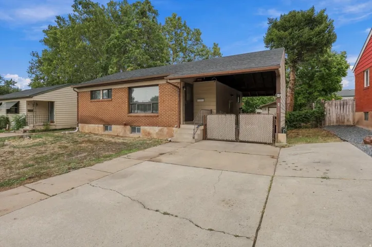 Brick exterior with a covered carport, concrete driveway, and mature trees
