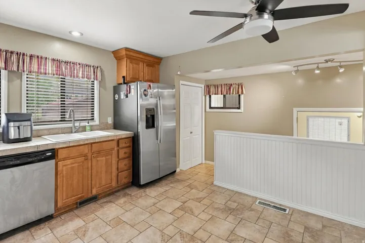 Kitchen featuring wood cabinetry, stainless steel appliances, a ceiling fan, and tile flooring