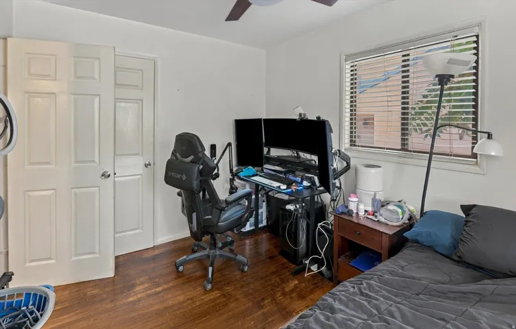 Wood-finish flooring with a ceiling fan, a window with horizontal blinds, and a built-in closet with panel doors