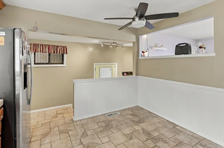 Tile flooring, white wainscoting, ceiling fan with integrated lighting, pass-through window, and built-in track lighting