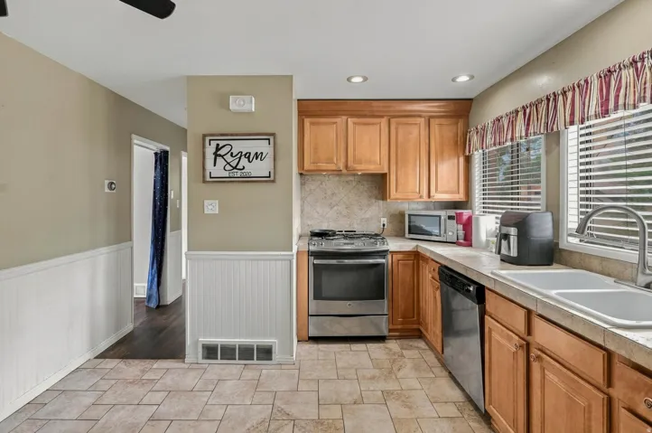 Kitchen featuring tile flooring, wood cabinetry, stainless steel appliances, and a double basin sink with a gooseneck faucet