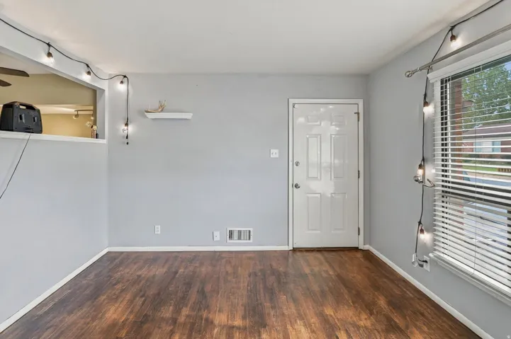 Wood-finish flooring with light gray walls, a white paneled entry door, and a single window with blinds