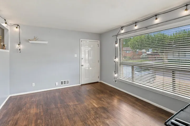 Wood-finish flooring throughout, bright window with blinds, and a white paneled entry door