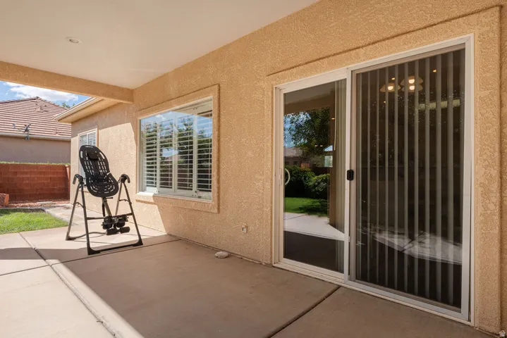 Covered patio with recessed lighting and concrete flooring, featuring a sliding glass door and a window with plantation shutters