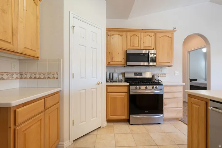 Wood-finish cabinetry, stainless steel microwave, gas range, tile backsplash with decorative accent, and tile flooring
