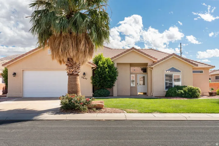 Stucco exterior with a tiled roof, mature palm tree, attached garage, and a covered entryway