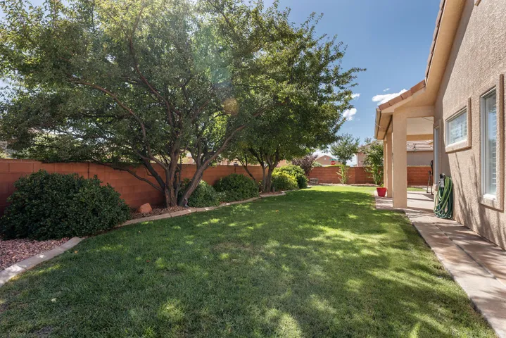 Expansive backyard featuring a lush lawn, mature trees, privacy fencing, and a covered patio area with textured stucco exterior