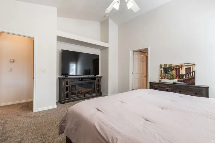 Vaulted ceiling with a ceiling fan, recessed entertainment niche, built-in electric fireplace, and light beige carpet