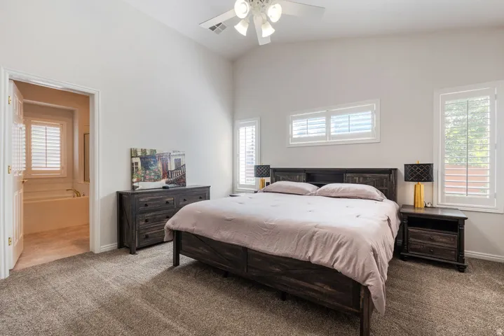 Vaulted ceiling with an attached ceiling fan, multiple windows with plantation shutters, and a carpeted floor