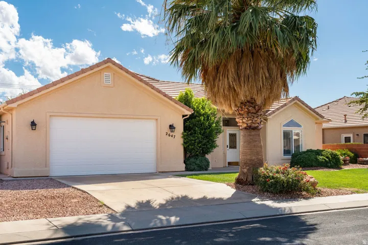 Stucco exterior with a tiled roof, attached garage, concrete driveway, and established landscaping