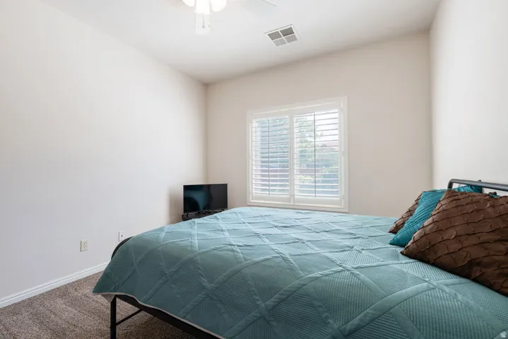 Window with plantation shutters, carpeted flooring, and a ceiling fan