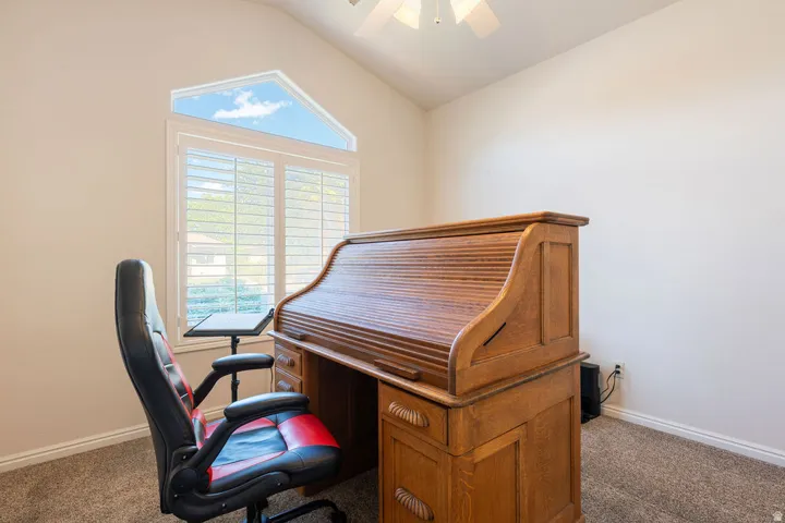 Vaulted ceiling with ceiling fan, triangular transom window, plantation shutters, and light-colored wall paint