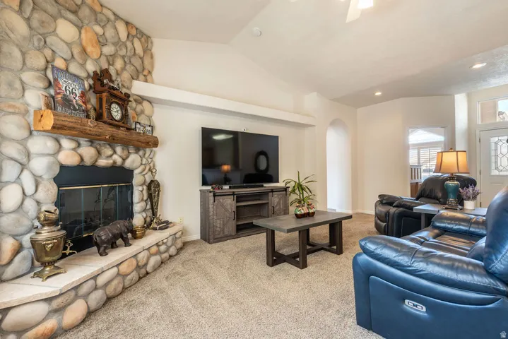 River rock fireplace with a wood mantle and hearth, vaulted ceiling, recessed lighting, arched doorway, and carpeted flooring