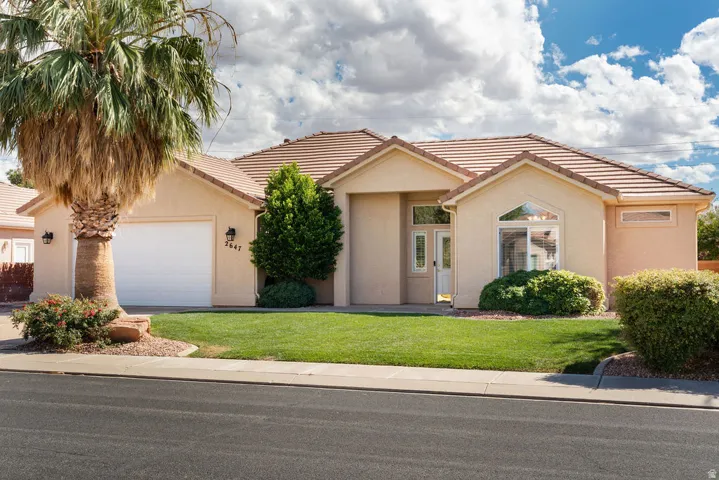 Stucco exterior with a tile roof, an integrated garage, a manicured lawn, and mature landscaping