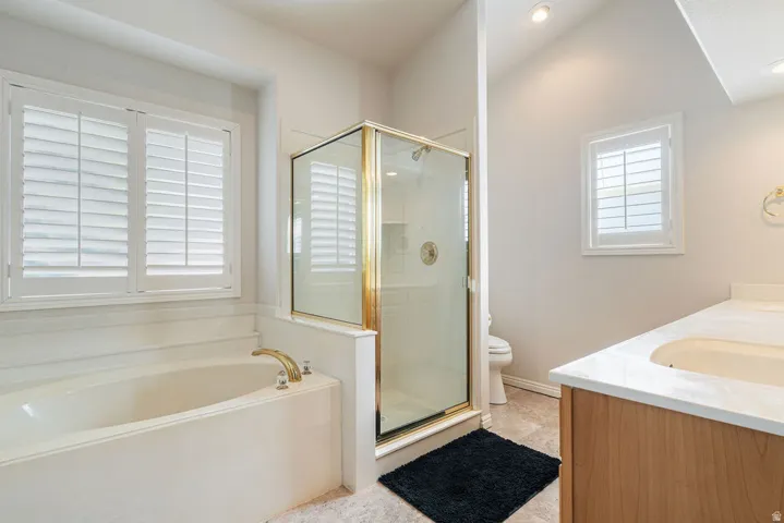 Soaking tub with brass fixtures, glass-enclosed shower with brass frame, and dual vanity with light-tone wood cabinetry and white countertop