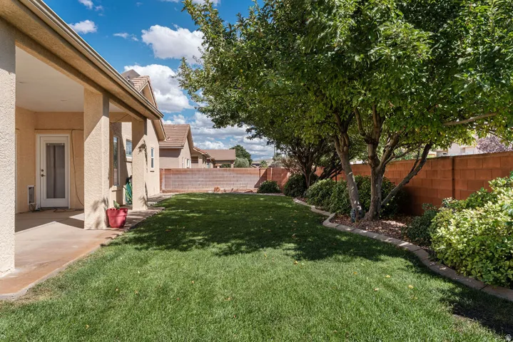 Expansive grassy yard with mature trees and a covered patio, bordered by a block wall fence