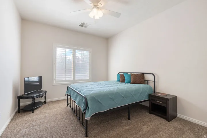 Carpeted flooring, white walls, window with white plantation shutters, and a ceiling fan with integrated lighting