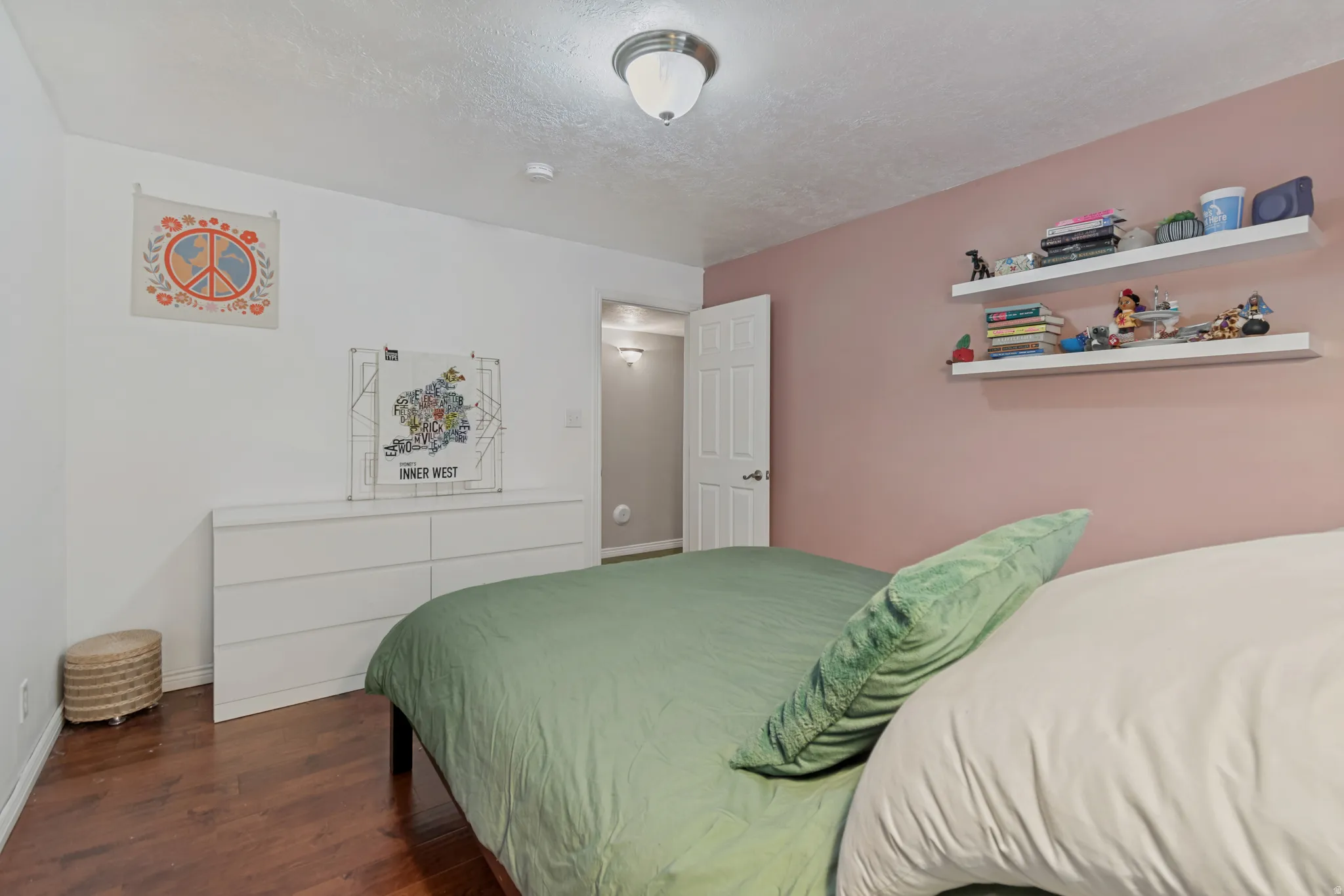 Wood-finish flooring with a white six-drawer dresser, two wall-mounted floating shelves, and a ceiling-mounted light fixture