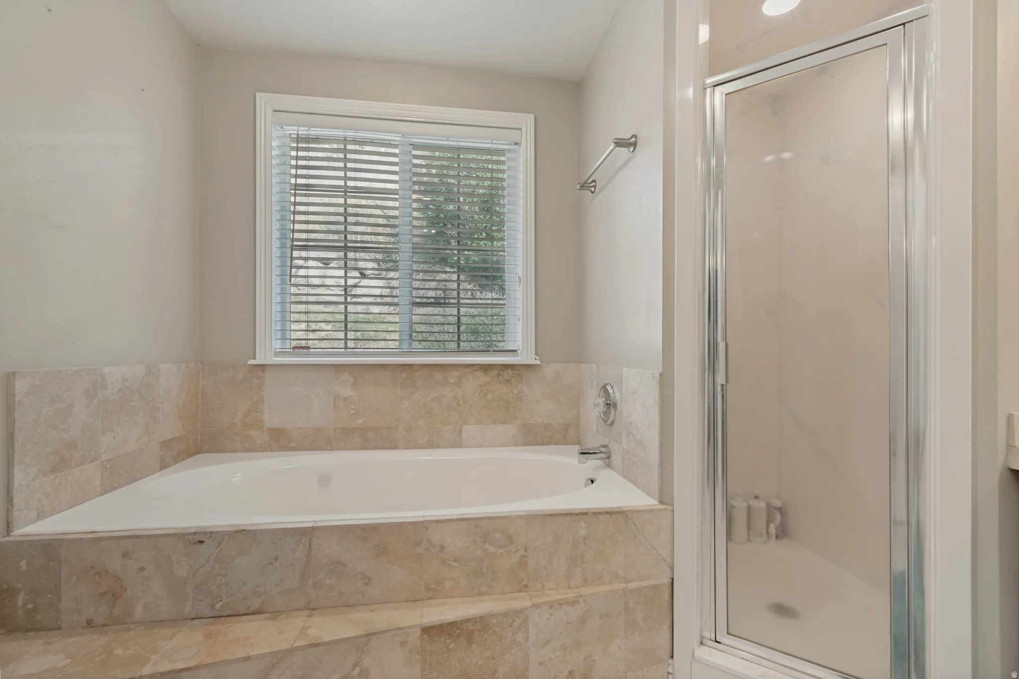 Built-in soaking tub with stone surround, complemented by a glass-enclosed shower with a chrome frame
