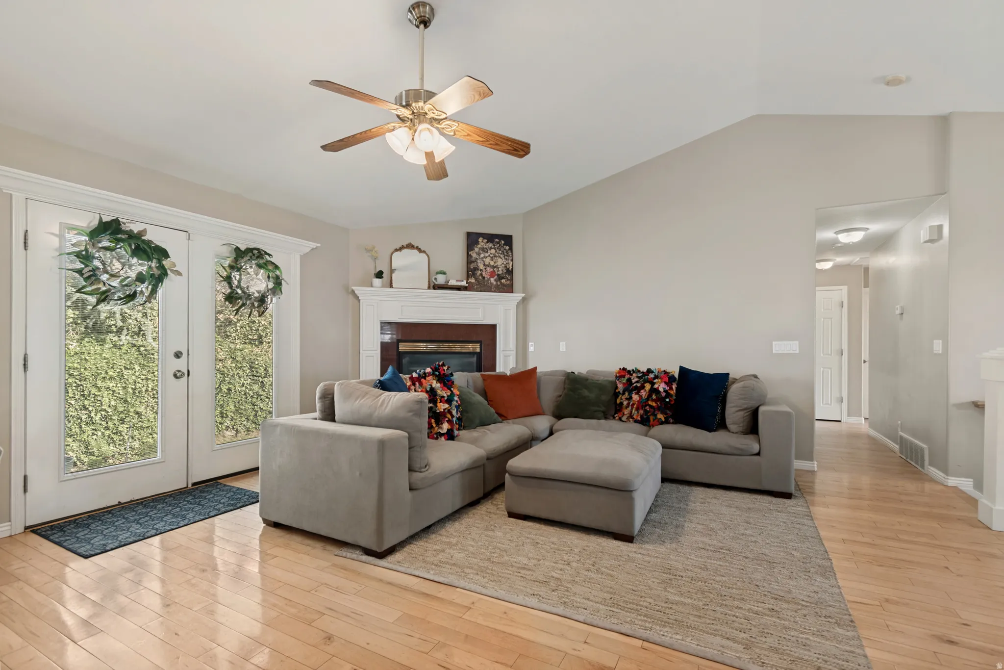 Vaulted ceiling, ceiling fan, fireplace with a white mantel, wood-finish flooring, and double glass-paneled doors