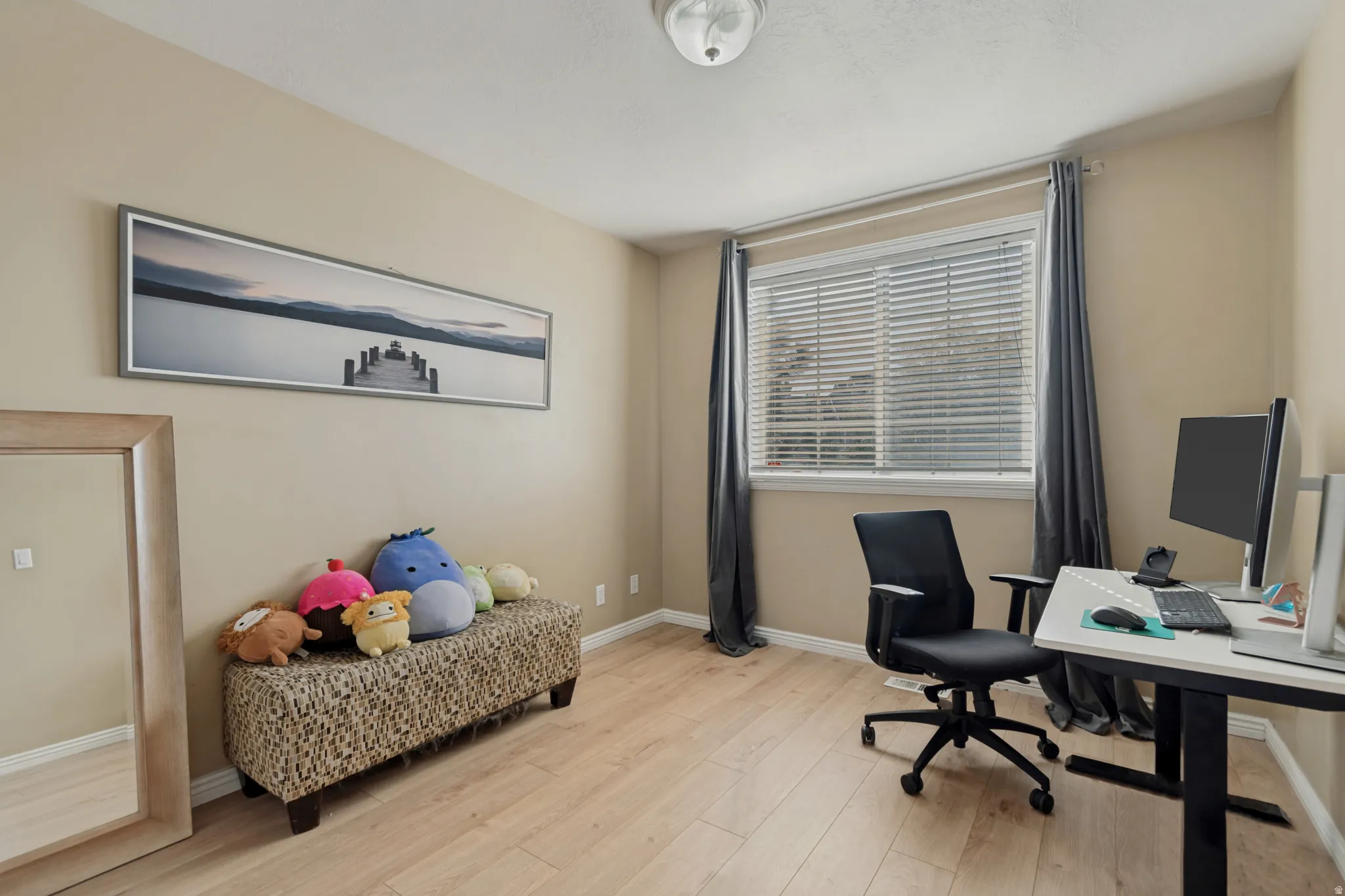 Light wood-finish flooring, neutral wall paint, window with blinds and drapes, and a ceiling-mounted light fixture