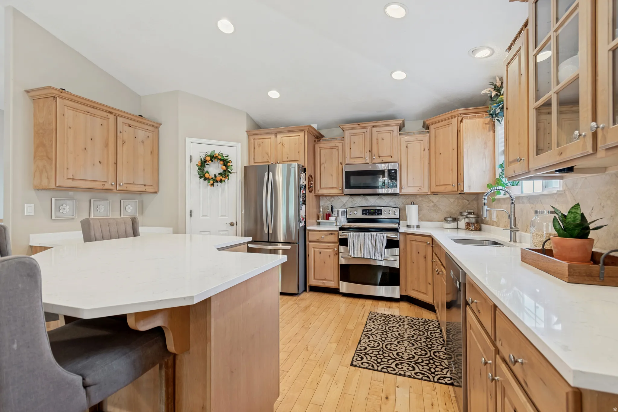 Vaulted ceilings, light wood-finish cabinetry, stainless steel appliances, white countertops, and wood-finish flooring