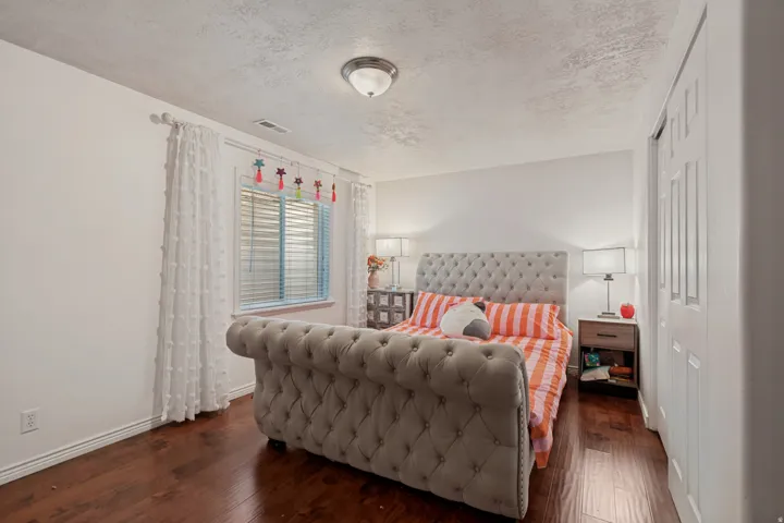 Wood-finish flooring with white baseboards, featuring a window with blinds, and white bi-fold closet doors