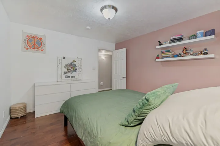 Wood-finish flooring with a white six-drawer dresser, two wall-mounted floating shelves, and a ceiling-mounted light fixture