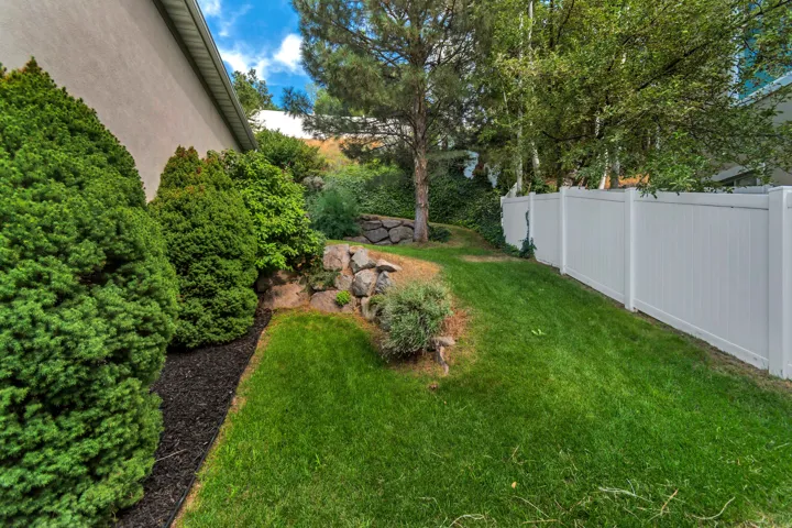 Expansive grassy area with a white privacy fence and established shrubbery