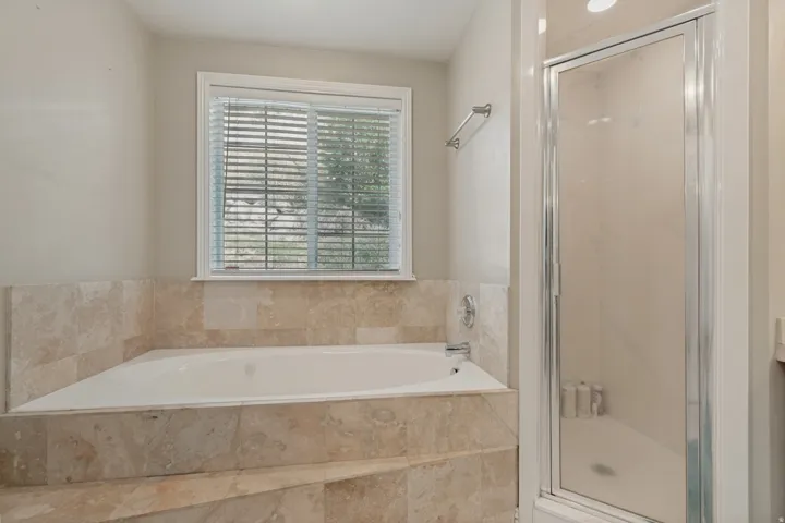Built-in soaking tub with stone surround, complemented by a glass-enclosed shower with a chrome frame