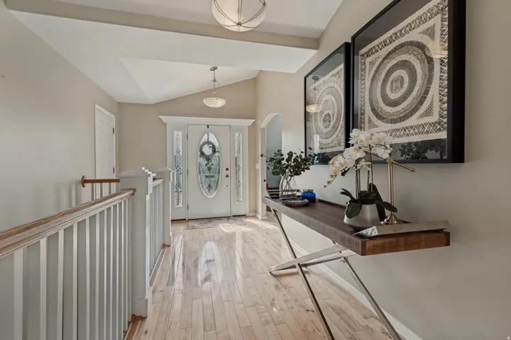 Vaulted ceilings, wood-finish flooring, white banister with natural wood handrail, arched entryway, and transom window with sidelights