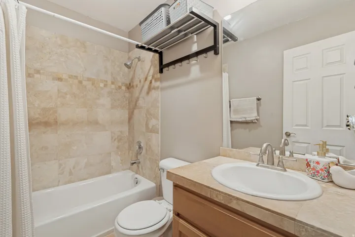 Tub/shower combination with tile surround, single vanity with integrated sink, and wood-finish cabinetry