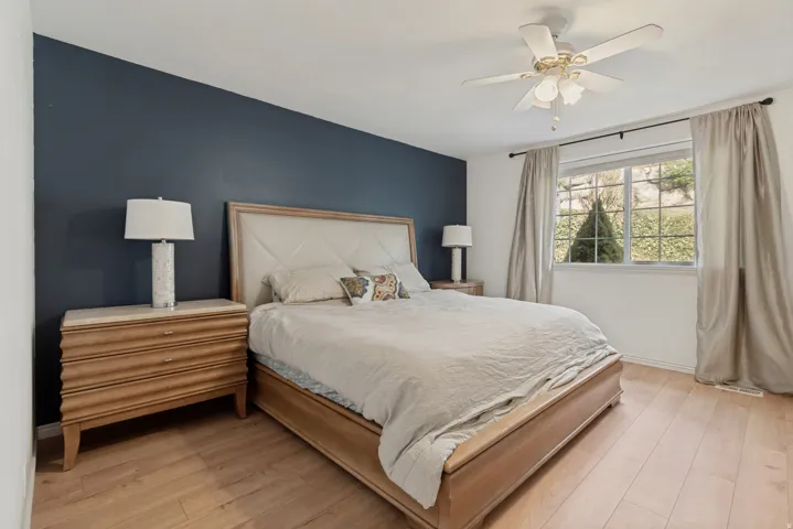 Wood-finish flooring, accent wall, ceiling fan, and large window with exterior scenery